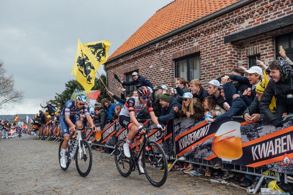 Tadej Pogačar and Mathieu van der Poel ride clear at the Tour of Flanders in front of a huge crowd behind 'Kwaremont' advertising and Flanders yellow and black lion flags